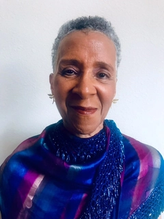 Holistic healing through Energy Kinesiology, Reiki, Aromatherapy, and more.. Reverend doctor Adara Walton smiling for a photo wearing a blue and purple silk blouse.